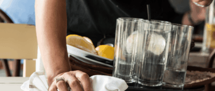 Server cleaning table with white cloth, holding tray of dishes