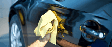 A man with a yellow cloth polishing a car